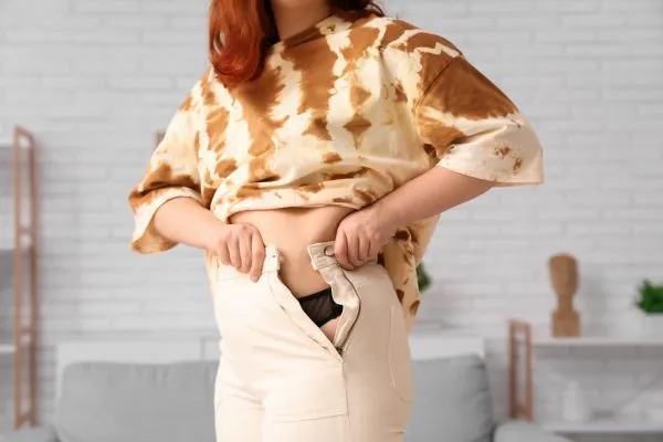 Image of woman trying to do her trousers up after pregnancy weight gain Langley